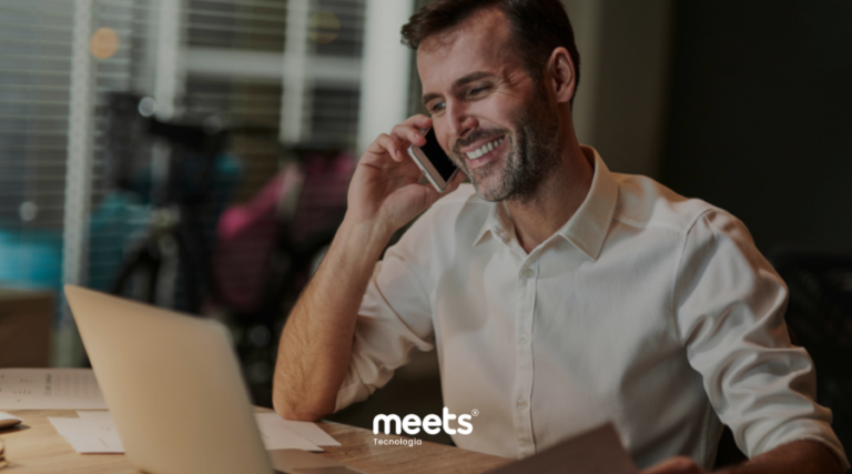 Profissional de vendas sorrindo enquanto fala ao telefone em frente a um laptop durante atendimento a um lead, em ambiente de trabalho.