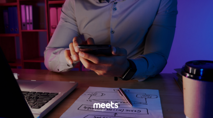 Profissional analisando estratégia de marketing no celular ao lado de laptop e planejamento de funil de vendas em papel, representando análise de orçamento de marketing e decisões baseadas em dados.