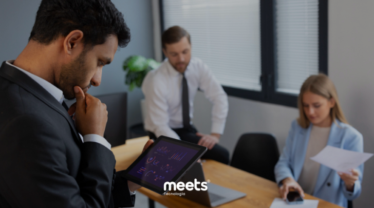 Gestor analisando dados em tablet enquanto equipe revisa documentos, representando o desafio de interpretar informações e tomar decisões em meio à sobrecarga de trabalho.