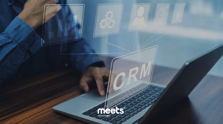 Uma pessoa usando um notebook sobre uma mesa de madeira, com elementos holográficos flutuantes que representam ferramentas de gestão e a palavra CRM em destaque. No canto inferior central, está o logotipo da Meets Tecnologia.